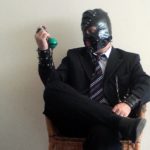Um executivo fetichista usando máscara de latex segurando gagball